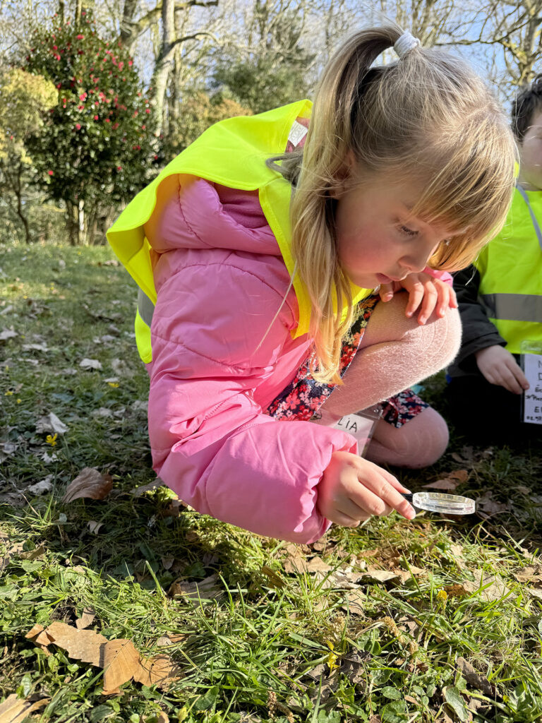 une petite fille regarde l'herbe a la loupe